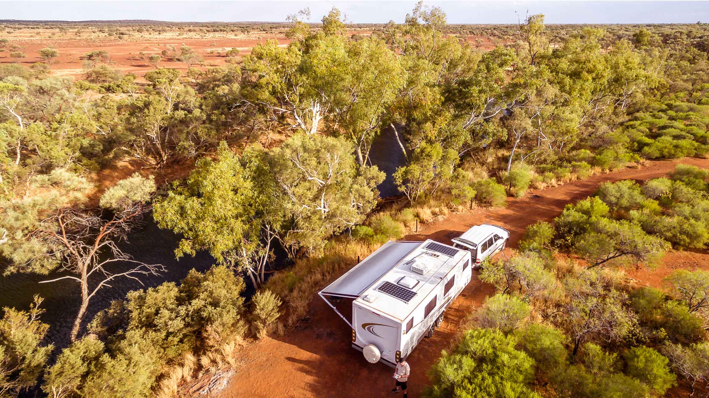 Camper van with solar panels parked up in the middle of the bush, red earth surrounds it with gumtrees.