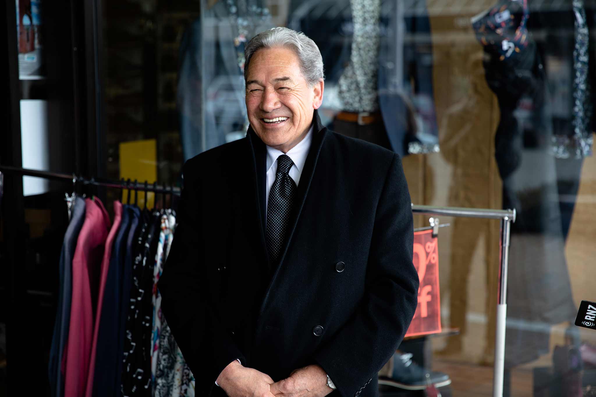 Photo of Winston Peters smiling and standing in front of a clothing store.