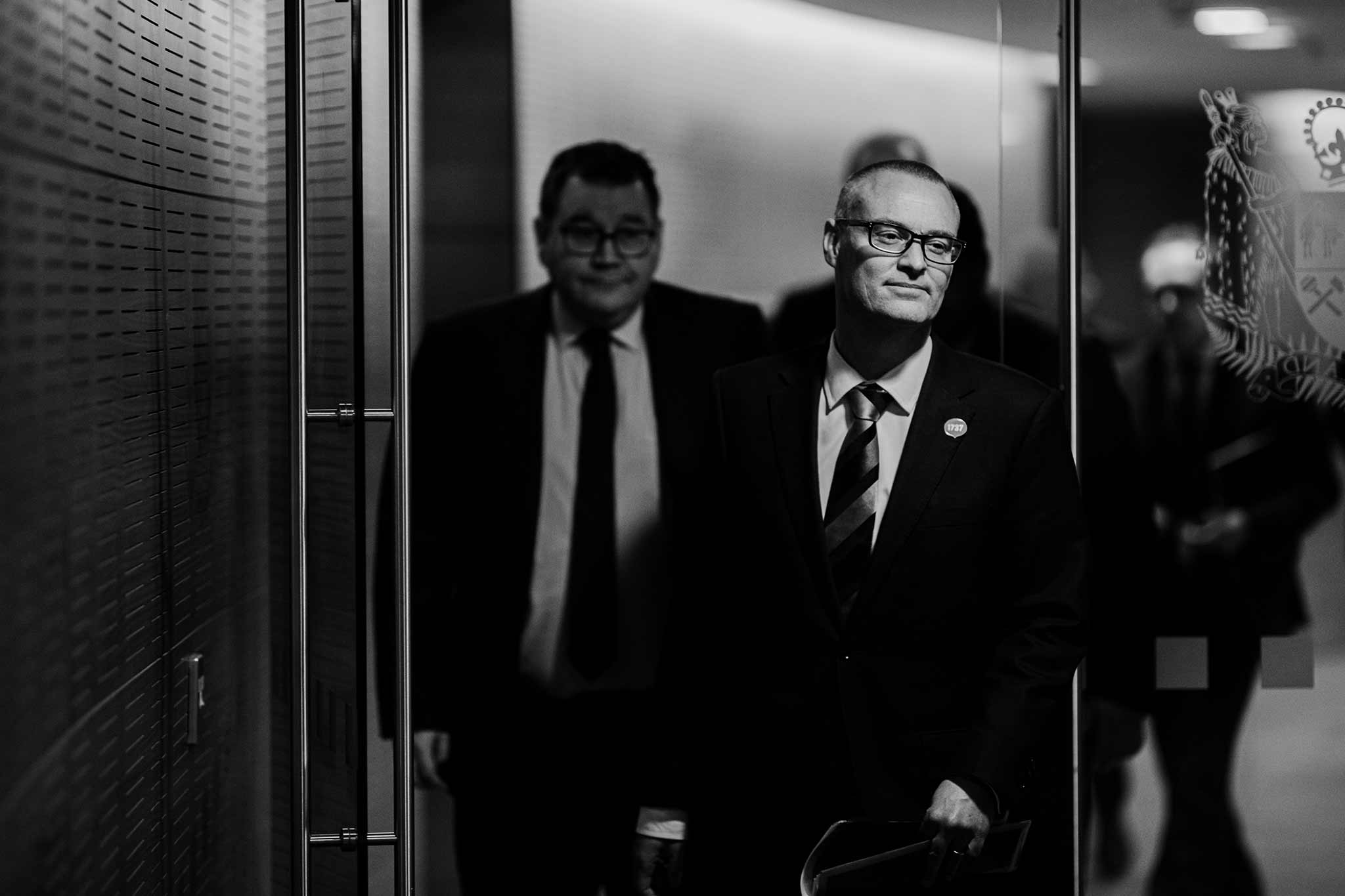 Black and white photo of David Clark walking through a doorway, followed by Grant Robertson.