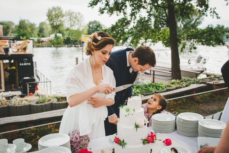 The bride is cutting her vegan wedding cake whilst the groom chats to a young flower girl
