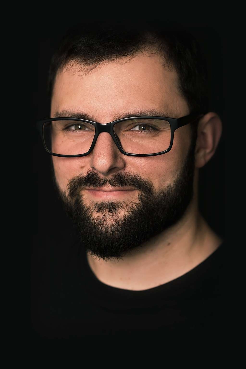 headshot of Matthew Basile wearing glasses and a black shirt photographed on a black background.