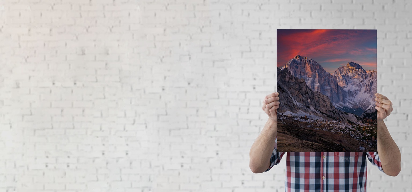 A man holds a stretched canvas printed with a vibrantly colored landscape image 