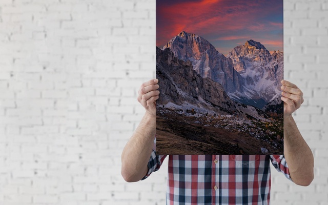 A man holds a stretched canvas printed with a vibrantly colored landscape image 