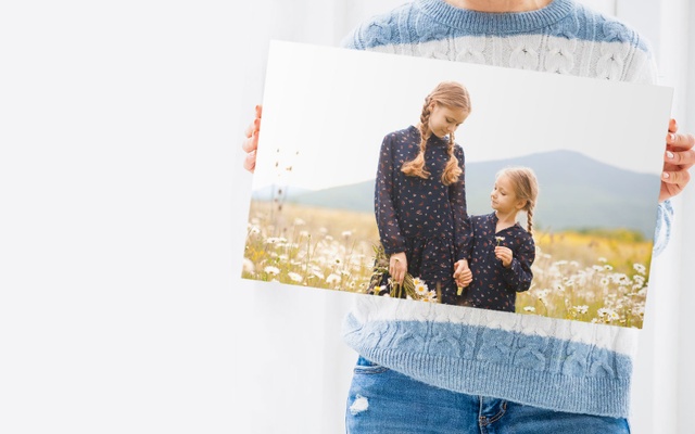 A woman holds a canvas featuring a candid photo of her daughters playing in a field
